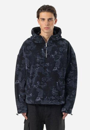 Musta fleece-pullove, jossa on huppu, neljännesvetoketju edessä ja sävysävyyn abstrakti kuvio. Vaatteessa on logopatchi rinnassa ja säädettävät hihansuut.