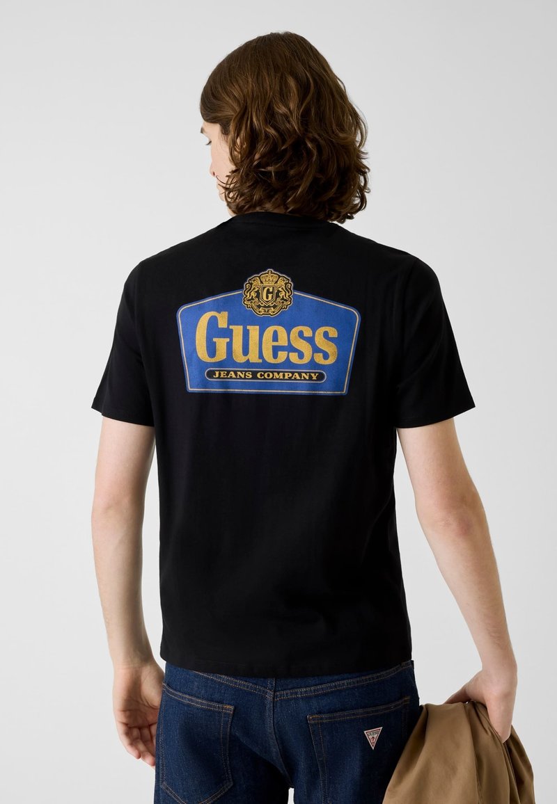 Czarny t-shirt z dużym, niebiesko-złotym logo "Guess Jeans Company" na plecach. Wykonany z miękkiej tkaniny, z klasycznym, okrągłym dekoltem.