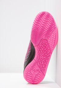 Vaaleanpunainen kumipohja, jossa on siksak-kuvio, rakenteellinen pito ja geometriset yksityiskohdat; kudottu musta ja vaaleanpunainen päällinen tarjoaa kontrastoivan muotoilun.