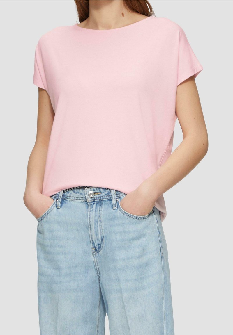 Jasnoróżowa bluzka z krótkim rękawem i okrągłym dekoltem, zestawiona z jasnoniebieskimi dżinsami. Materiał wydaje się miękki i ma luźny krój.