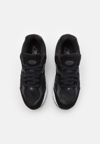 Chaussures de sport noires avec une tige en mesh et en daim, des accents gris, un col rembourré et une semelle intermédiaire blanche.