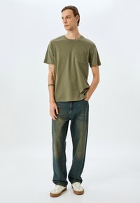 Olivenfarvet bomulds t-shirt med brystlomme, parret med løstsiddende, lyseblå jeans og hvide sneakers med brune såler.