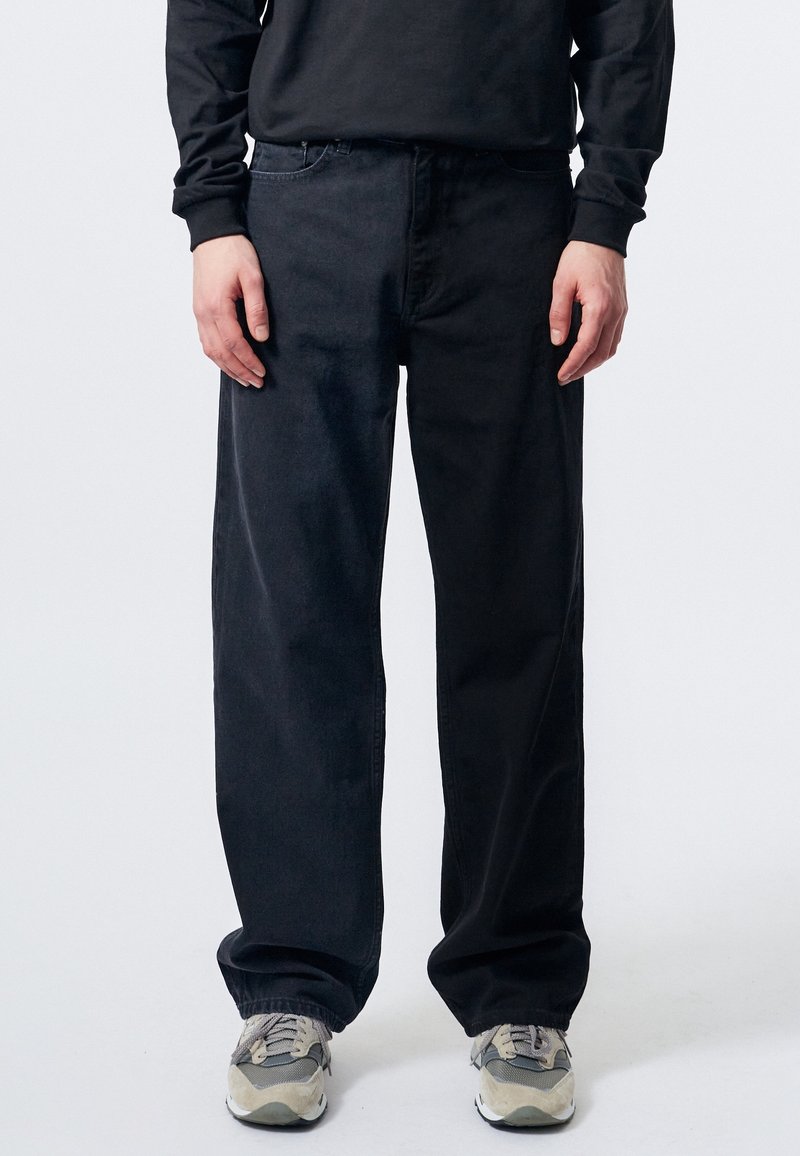 Černé džíny z denimu s volnějším střihem, se klasickým pětipocket designem a prošitím, v kombinaci se šedými teniskami.