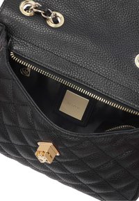 Sac à main en cuir matelassé noir partiellement ouvert montrant une fermeture éclair dorée, une boucle de sangle en chaîne dorée et une plaque de marque dorée à l'intérieur.