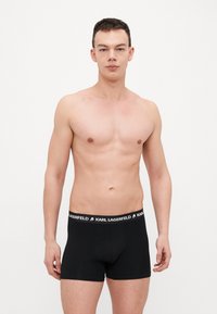 Melnas bokseru apakšbikses ar mīkstu struktūru un elastīgu jostu, uz kuras ir balts "KARL LAGERFELD" logo, paredzētas ciešai piegulšanai.