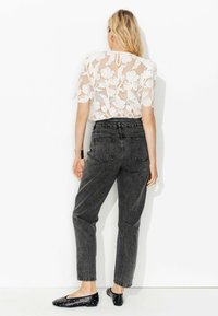 Haut en dentelle blanche avec motifs floraux, associé à un jean gris foncé taille haute. Des ballerines noires à clous argentés complètent la tenue.