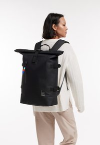Svart rulltoppsryggsäck med justerbara remmar, strömlinjeformad form, vattentåligt material och minimal varumärkning på framsidan för en modern look.