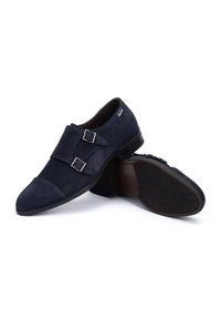 Zapatos de ante azul marino con herrajes de doble hebilla, punta afilada y suela de goma texturizada. Acabado liso con acentos de costura.