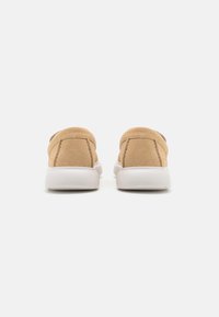 Beige suède instappers met een ronde achterkant, voorzien van een witte rubberen zool. Glad textuur met nette stiksels.