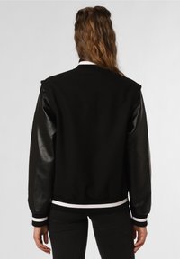 Černá varsity bunda se solidním vlněným tělem a lesklými černými koženými rukávy. Obsahuje bíle pruhovaný ribbed pas a límec.