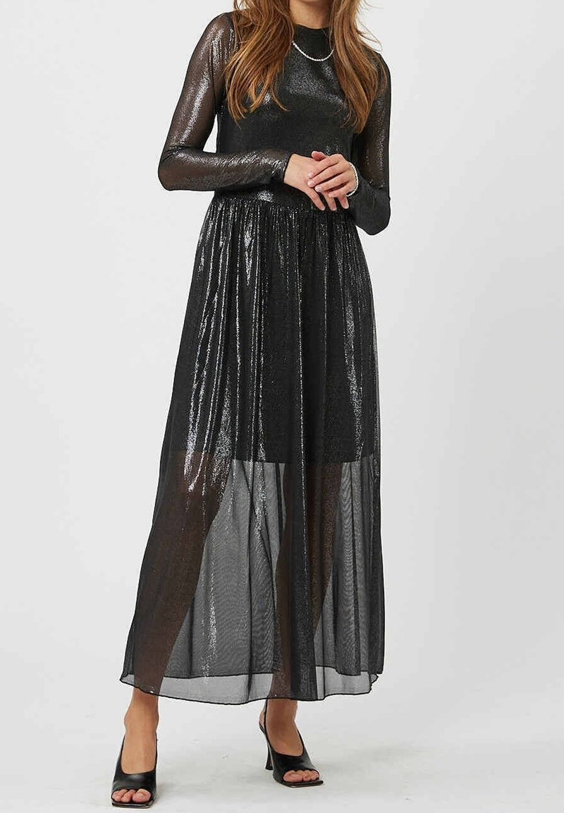 Robe de soirée noire avec manches longues transparentes, corsage ajusté et jupe fluide semi-transparente. La texture présente des reflets scintillants.