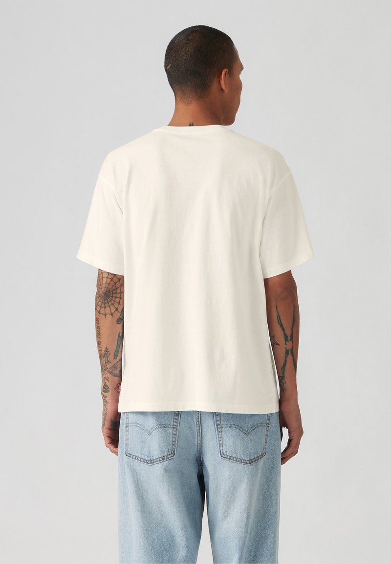 Kortärmad vit bomullströja med klassisk passform, med rund halsringning och en oredigerad baksida, i kombination med ljusblå jeans.