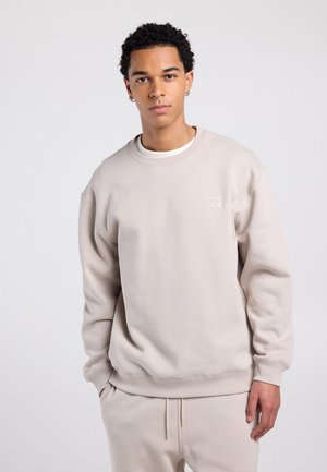 Lichtbeige sweatshirt gemaakt van zachte stof, met een ronde hals, geribbelde manchetten, een minimalistisch logodetail op de borst en een ontspannen pasvorm.