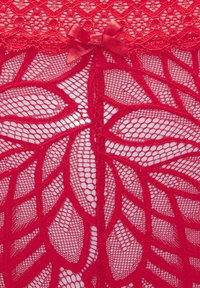 Sarkana mežģīņu apakšveļa ar lapu rakstu, kurai ir sarežģīta acu detaļas, centrāla atvēršana un neliela loku apdare augšpusē.