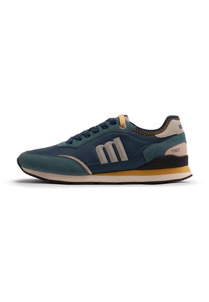 Zapatilla casual en azul marino y turquesa con acentos beige y amarillos, con un gran logo de "M" y "1967" en la contrafuerte del talón.