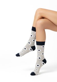 Calcetines grises con patrones circulares de ojos en blanco y negro, con puño y puntera acanalados de color azul oscuro, de longitud media hasta la pantorrilla. Textura de tela suave.