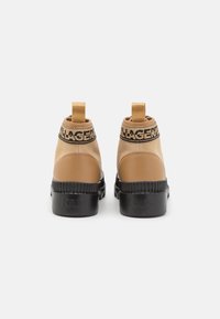 Stivaletti color cuoio con suola nera, dotati di una fascia elastica con logo. Il design presenta pelle liscia e un pannello posteriore testurizzato.