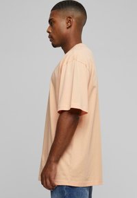 T-shirt pêche clair à manches courtes, coupe décontractée et col rond. Tissu en coton doux avec coutures latérales visibles.