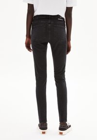 Jean skinny en denim foncé, avec une taille mi-haute, un design à cinq poches et des coutures contrastantes. Porté avec des baskets basses noires.