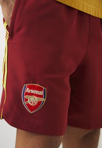 Bordeaux atletiske shorts med gule detaljer, med et fremtredende brodert Arsenal-logo. Glatt stoff og tilpasset passform, med sidelommer.