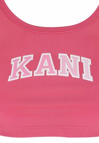 Roosa spordirinnakangas ribatekstuuriga, millel on valged tähed, mis kirjutavad "KANI". Ümar kaelus ja laiad rihmad, ilma lisamustrite või detailideta.