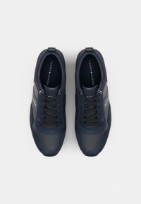Granatowe trampki z gładkiego materiału syntetycznego, wyposażone w czarne sznurówki, gumową podeszwę oraz biały pasek z logo po boku.