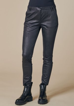 Schwarze Kunstlederhosen mit Slim-Fit, ausgestattet mit Vordertaschen und einer glatten Textur. Kombiniert mit schwarzen Stiefeletten.