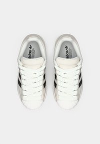 Λευκά αθλητικά παπούτσια με μαύρες ρίγες, λαστιχένια μύτη και λευκά κορδόνια. Απαλό ανώτερο υλικό, μαλακός γιακάς και ανάγλυφο λογότυπο στο εσωτερικό.