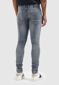 Verbleekte blauwe skinny jeans met een gladde textuur, vijf zakken en een merknaam op de tailleband, gecombineerd met witte en grijze sneakers.