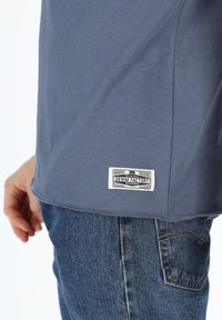 T-shirt in cotone blu con orlo arrotondato e un'etichetta "DENIM FACTORY" in basso a destra, abbinata a jeans in denim blu sbiadito.