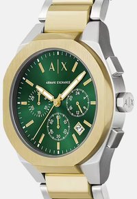 Reloj de acero inoxidable dorado y plateado con esfera verde, acentos dorados, tres subesferas, indicador de fecha y diseño de caja octagonal.