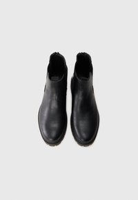 Botas de cuero negro hasta el tobillo con punta redondeada, una textura suave y cremalleras laterales para facilitar su uso. Suela resistente con un patrón de relieve mínimo.