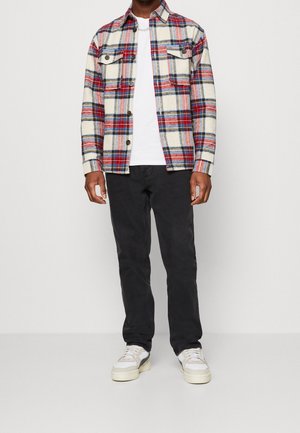 Kostkovaná fleece košile v krémové, červené a modré barvě; bílý tričko; černé kalhoty; světlé tenisky. Košile na knoflíky se dvěma kapsami na hrudi.