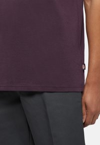 Lila kortärmad t-shirt med en mjuk textur, med en sidetikett, ihop med grå byxor. Ren design, inga synliga mönster.