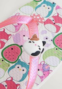 Flip-Flop mit einem strukturierten, pinken Riemen, der mit einem Katzenaugen-Detail verziert ist. Die Sohle hat ein Pastellmuster von Tieren und Früchten auf einem weißen Hintergrund.