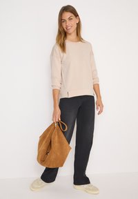 Sweatshirt beige clair à coupe décontractée, manches trois-quarts et fentes sur les côtés, associé à un jean noir et un sac en suède marron.