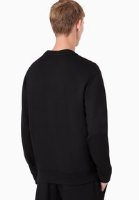 Felpa nera con collo rotondo e maniche lunghe, caratterizzata da una texture liscia e un'etichetta rettangolare sul retro del collo.