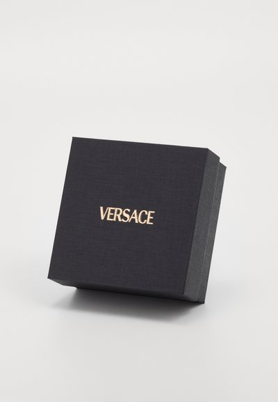 Melnas teksturētas taisnstūra kastes ar vāku, kurai priekšā ir zelta "VERSACE" logo. Minimālistisks dizains, elegants izskats.
