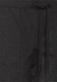 Joggers neri in tessuto testurizzato con vita regolabile tramite cordino, caratterizzati da un sottile motivo a spina di pesce e un tessuto morbido. Accentuati da punte in metallo nero.