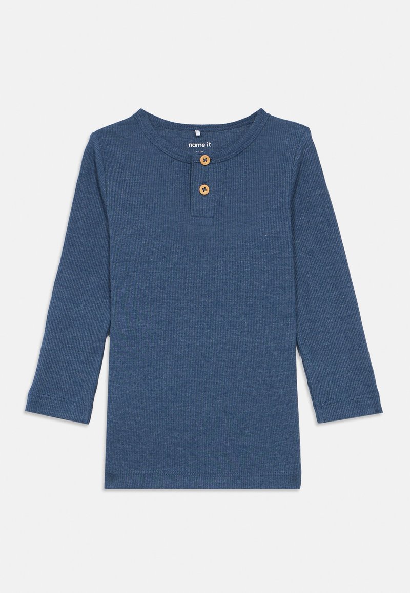 Camisa de manga longa canelada em azul escuro com decote henley e dois botões de madeira. O material é algodão macio com um acabamento texturizado.