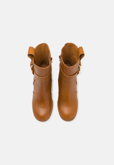 Brune læder ankelstøvler med en glat tekstur, der har en udvendig lynlås, spændeaccent og et rundt tådesign. Flad gummisål.