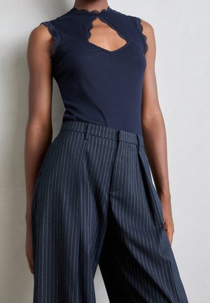 Haut sans manches côtelé bleu marine avec un col festonné et un détail découpé, associé à un pantalon large à fines rayures dans des tons foncés assortis.