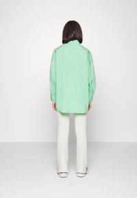 Camisa oversized verde menta com mangas longas, bainha arredondada e detalhes em botão, combinada com calças flare, em verde claro, com textura canelada.