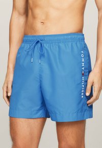 Costumi da bagno blu con vita elasticizzata e cordoncino. Presenta il logo bianco "TOMMY HILFIGER" di lato. Materiale liscio e leggero.