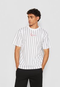 White short-sleeve t-shirt featuring vertical black stripes and a red script logo on the chest. Soft fabric with a relaxed fit.