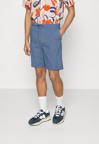 Shorts bleu clair en tissu doux, dotés d'une taille élastique avec cordon de serrage. Associés à des chaussettes blanches et à des baskets marines.