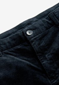 Pantaloni negri din corduroy, cu o textură netedă, model în dungi și un nasture cu patru găuri la talie. Detaliu cu fermoar vizibil.