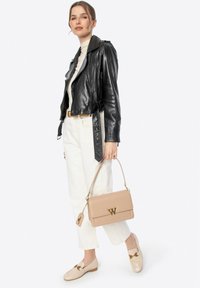 Schwarze Leder-Bikerjacke, cremefarbener Rollkragenpullover, weiße weite Hosen, beiger Handtasche mit goldenen Beschlägen und beigen Loafers mit dekorativem Akzent.