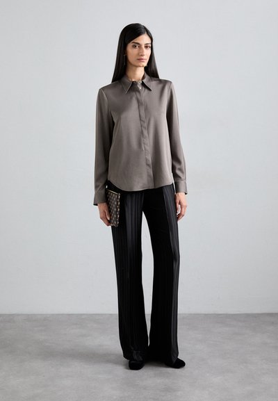 Satin, long-sleeve blouse in taupe with a button-down collar; paired with black pleated trousers and a patterned clutch.