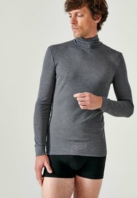 Maglione grigio a maniche lunghe con colletto a lupetto realizzato in un tessuto liscio e elasticizzato. Presenta una vestibilità attillata e polsini a coste, indossato sopra della biancheria intima nera.